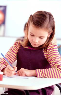 Primary aged girl sat at school desk writing Primary aged girl sat at school desk writing