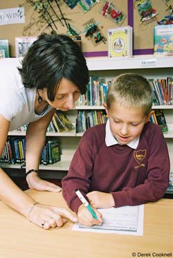 school boy completing work sheet aided by teacher